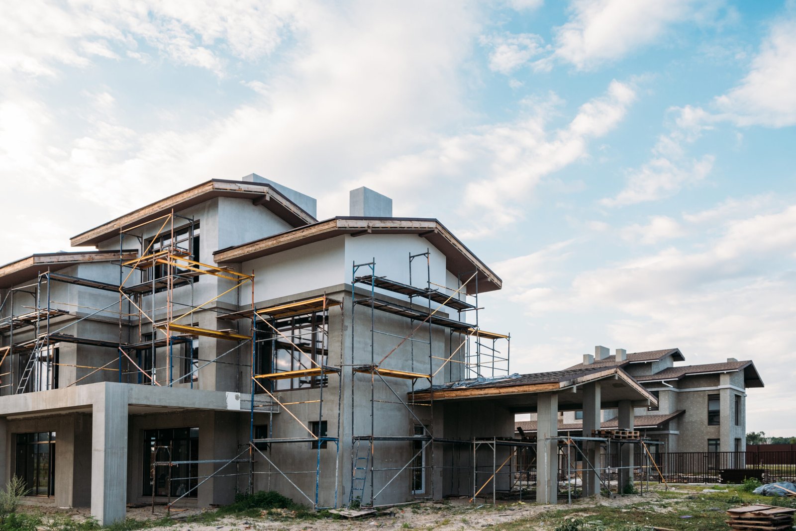 Casa de dois pavimentos em construção, cercada por andaimes metálicos, com estrutura e reboco em andamento.