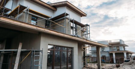 Casas modernas em construção com andaimes e janelas instaladas, etapa de reboco em andamento.